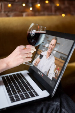 Weinberatung vom Sommelier und Weinhandel online mit Notebook. Kunde und Sommelier heben online ein Weinglas und prosten sich zu.
